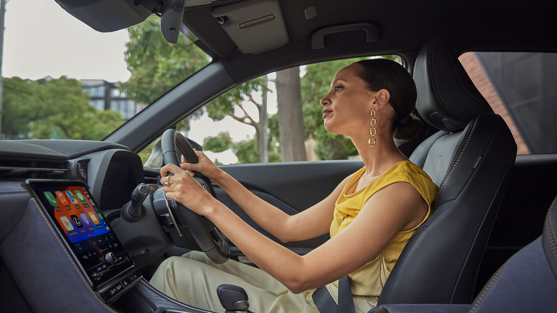 Woman is sat within a Lexus LBX, driving through a leafy green area. 