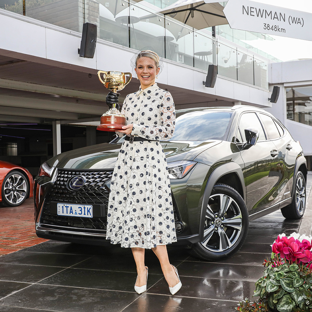 Emma Freedman holding the Lexus Melbourne Cup trophy and standing in front of a Lexus UX at Flemington racecourse 